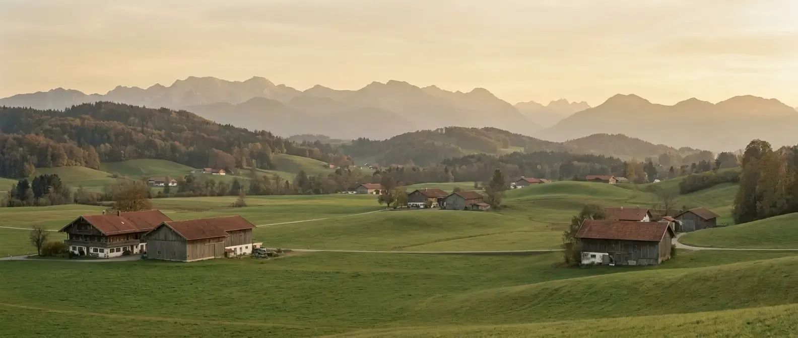 Voralpen-Landschaft bei Glonn — sanfte grüne Hügel mit Bauernhöfen, dahinter die Alpen im warmen Nachmittagslicht
